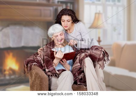 daughter and elderly mother charming read the book in the room with fireplace. grandmother