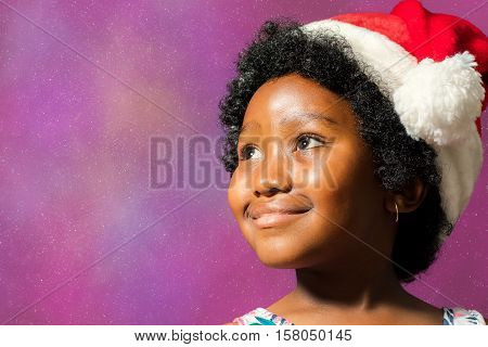 Close up face shot of little african girl wearing christmas hat. Kid staring at upper corner against starburst background.
