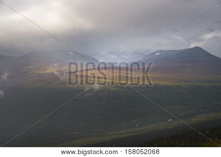 Sunlight giving golden colors to autumn forest with mountain and moody cloudscape background