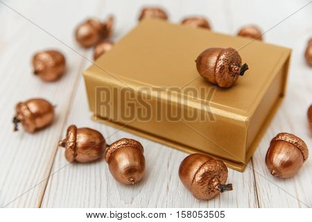 Christmas composition.Golden present box and golden acorns.White wooden table.Mokup with space.Selective focus