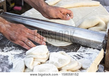 Chef making dough pastry sheeter at bakery Baker forming shaping dough rolled pastry metal work table closeup hands process of preparing bread khinkali dough roller machine thin pasta sheet Top view
