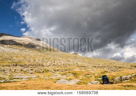 Backpack and walking sticks left to rest on a mountain with clouds overhead