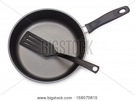 Black frying pan with cooking utensils: plastic paddle isolated on white background close-up top view.