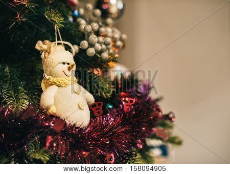Closeup of tinsel and a snowman ornament hanging from the branches of a Christmas tree in a home during the festive season