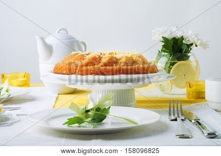 Yellow summer table setting with lemon bundt cake white plates teapot and chrysantemum flowers in a glass vase