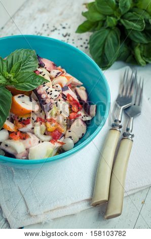 Fresh salad with seafood tomatoes and basil in a blue bowl on white rustic wooden background. Salad with squid octopus shrimp mussel and black sesame seeds. Seafood concept. Selective focus.