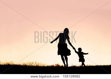 Silhouette Of Mother And Baby Daughter Running And Dancing At Sunset