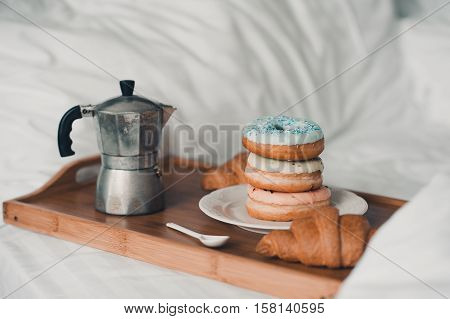 Stack of glazed donuts with croissant and coffee turk on wooden tray in bed. Good morning. Tasty breakfast. Selective focus.