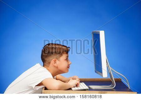 School-age boy sitting in front of the monitor laptop at blue studio backgroubd