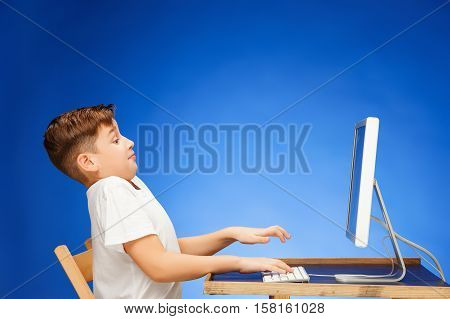 School-age boy sitting in front of the monitor laptop at blue studio backgroubd