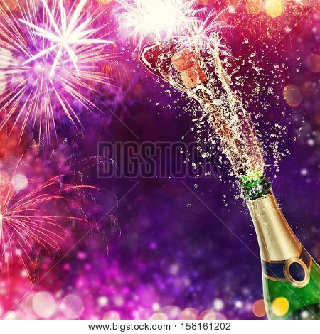Splashing bottle of champagne with glasses over blur colored background. Celebration concept, free space for text