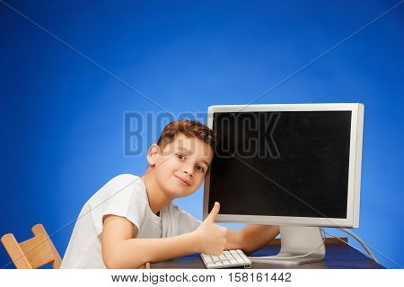 School-age boy sitting in front of the monitor laptop at blue studio backgroubd