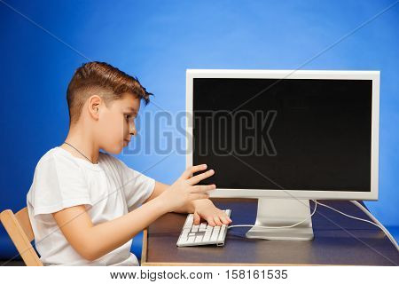 School-age boy sitting with the monitor laptop at blue studio backgroubd
