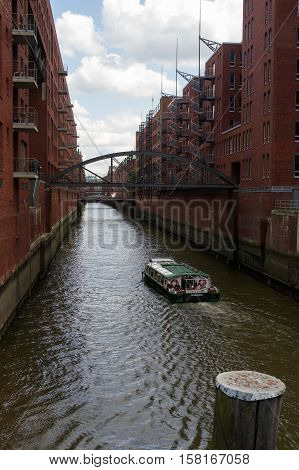 HAMBURG GERMANY - JULY 18 2015: a ferry on the canal of Historic Speicherstadt houses and bridges at evening with amaising skyview over warehouses famous place on Elbe river.