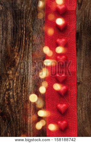 Hearts with bokeh and a red gift ribbon on a vertical wooden background for a concept