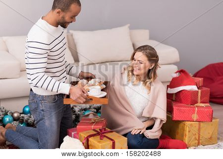 Expressing love. Nice handsome pleasant man holding a tray and offering his wife a breakfast while caring about her