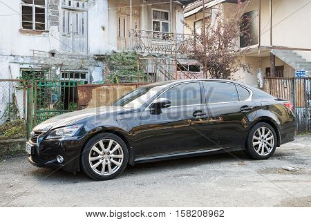 Sukhum, Russia - October 10, 2016: Lexus ES luxury sedan parked near a destroyed house where live poor people after the war with Georgia.