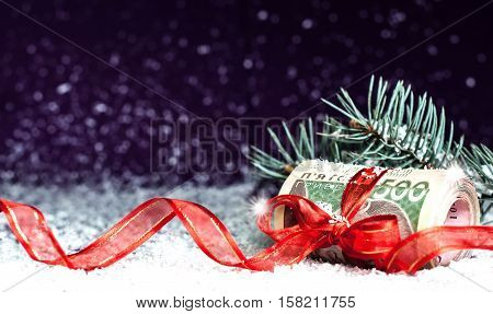 Roll of Ukrainian banknotes with red gift ribbon against the background of falling snow