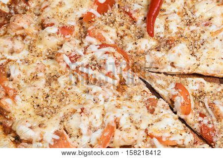 Mexican pizza with chicken tomatoes cheese and chili peppers in the middle closeup. Cut off one piece