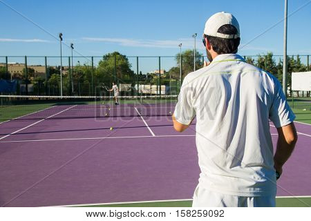 Professional tennis player playing the game on the tennis court. He has his back to the camera and have the racket in his right hand.