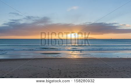 Sunrise on beach Waipu Cove sun breaking through low cloud on horizon glistening across sea