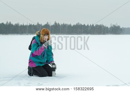 Winter hunkering hiker woman is drinking hot tea from vacuum flask metal cup