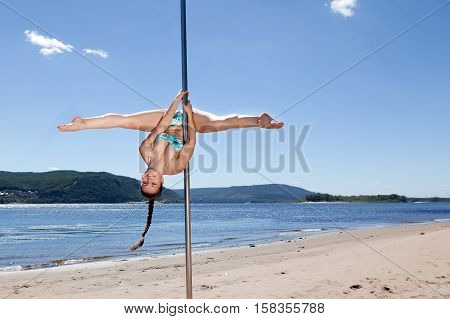 acrobatic performance laughing brunette woman in swimsuit on pole for dancing background of summer beach