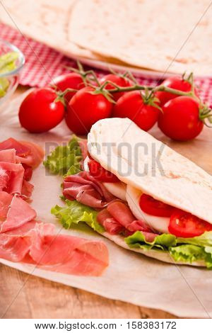 Piadina with ham and lettuce on wooden table.