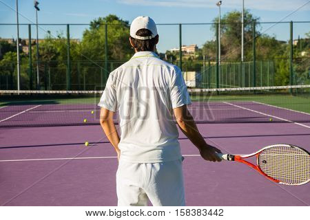 Professional tennis player playing the game on the tennis court. He has his back to the camera and have the racket in his right hand. He is in the center of the image.