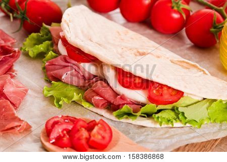 Piadina with ham and lettuce on wooden table.