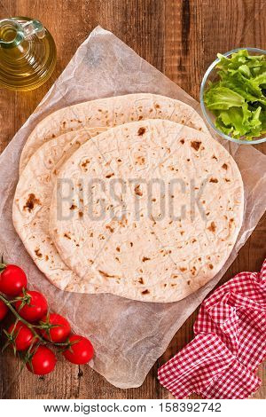Piadina with ham and lettuce on wooden table.