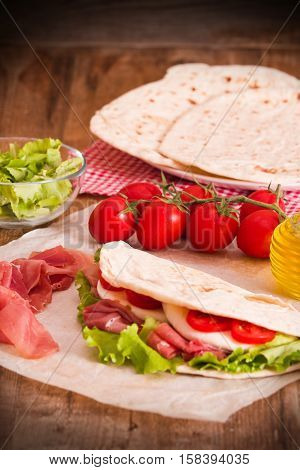 Piadina with ham and lettuce on wooden table.