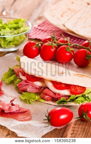 Piadina with ham and lettuce on wooden table.