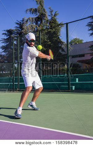 Professional tennis player playing a game of tennis on a court. He is about to hit the ball with the racket. The ball is suspended in the air.
