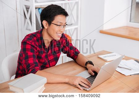 Picture of cheerful male student with laptop and books working in university. Looking at laptop.