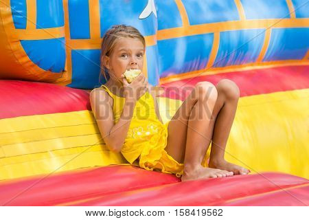 Girl Sits At The Entrance To An Inflatable Trampoline And Eating An Apple