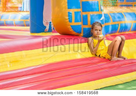 Girl Sits At The Entrance To An Inflatable Trampoline And Eats An Apple