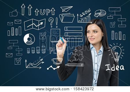 Close up of a woman with black hair drawing a business idea sketch on a glassboard in a blue room