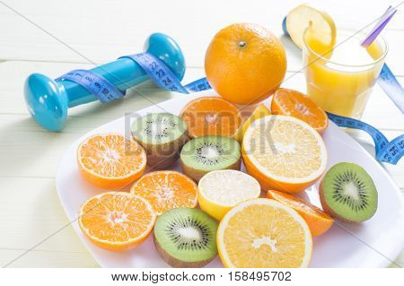 The concept of healthy lifestyle. Orange juice fruits. cereal bars dumbbell and measuring tape on yellow wooden table. Cereals and fruits - diet and breakfast