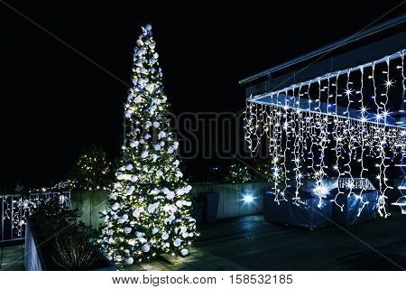 Ornate and lighted Christmas tree in the garden. Ornate and lighted Christmas tree in the garden. Xmas tree and lighting of the house at Christmas time