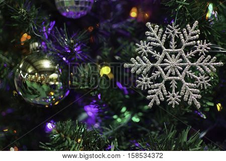 Snowflake ornament hanging on Christmas Tree with colored lights.