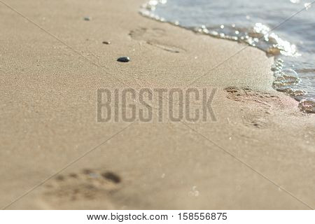 Footprints on a sandy beach close-up, in the right corner of the blue wave