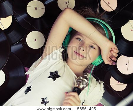 Beautiful girl lying next to vinyl records holding a microphone and listening music on headphones.Top view.