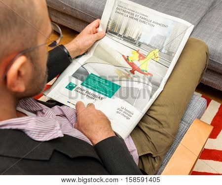 PARIS FRANCE - NOV 12 2016: Man reading Le Figaro French newspaper - reading advertising of BNP Paribas bank - one ot he biggest banks in France