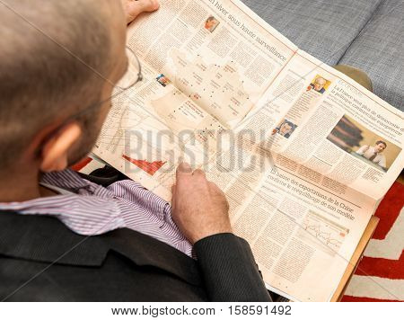 PARIS FRANCE - NOV 12 2016: Man reading Le Figaro French Economie newspaper about nuclear plants in France and pointing to their location on map