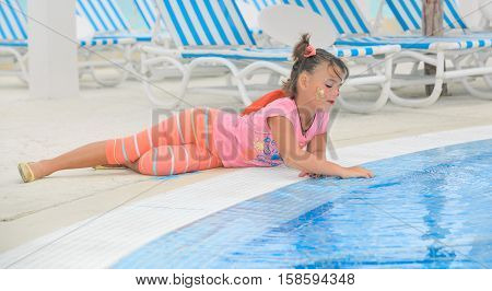 beautiful little girl laying down at the pool edge and softly touching the water