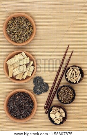 Traditional chinese herb ingredients used in alternative medicine, i ching coins and chopsticks over bamboo background.