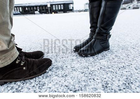 Male and Female casual boots standing on asphalt covered gritty snowY surface. Rough snowy surface. Textplace. Cold Winter. Side view