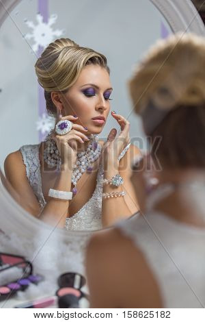 Beautiful young woman with bright purple makeup and fancy hairdo sitting in front of mirror. Gorgeous winter bride.