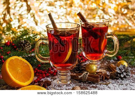 hot christmas mulled wine with golden bokeh background, snow, cinnamon sticks, anise and orange on wooden table background with fir branches and pine cones. soft focus. shallow depth of field